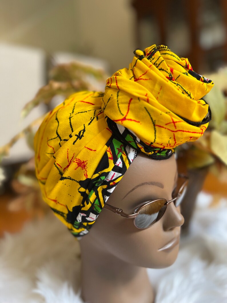 May include: A yellow head wrap with a black and white geometric pattern. The wrap is tied in a knot on top of the head.