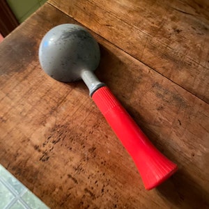 May include: A silver ice cream scoop with a red plastic handle. The scoop is on a wooden surface.