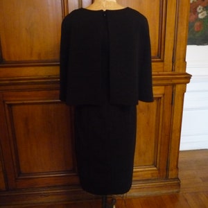 May include: A black dress with a cape-like top and a knee-length skirt.