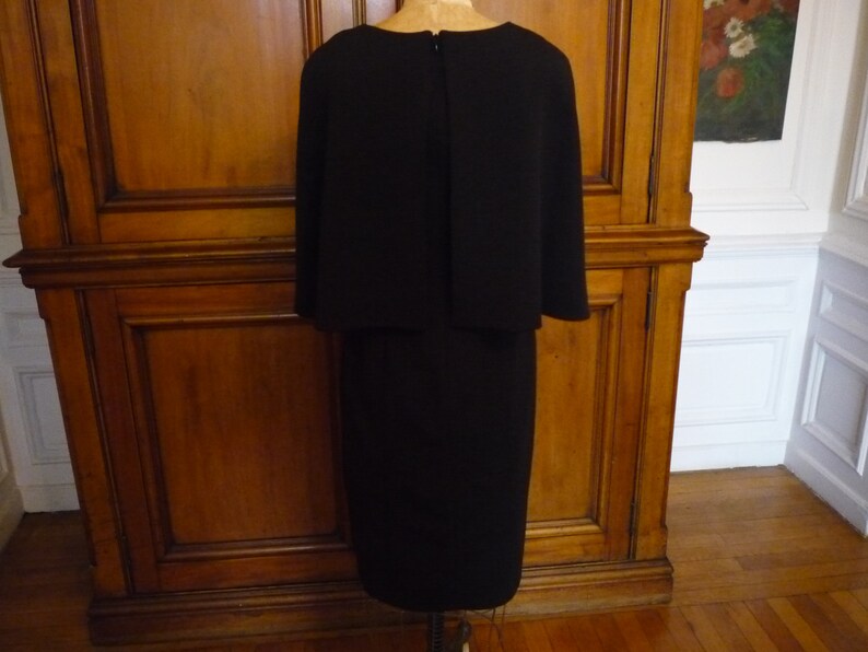 May include: A black dress with a cape-like top and a knee-length skirt.