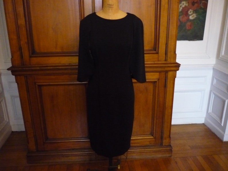 May include: A black, knee-length dress with a simple, fitted silhouette and three-quarter sleeves.