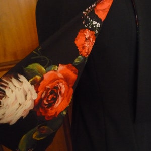 May include: A black blazer with a floral print lining. The lining features red roses, white flowers, and green leaves on a black background.
