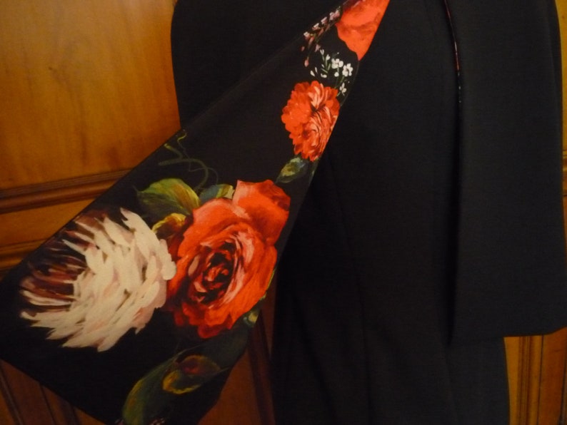May include: A black blazer with a floral print lining. The lining features red roses, white flowers, and green leaves on a black background.