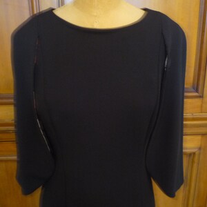 May include: A black dress with long sleeves and a round neckline. The sleeves have a unique design with a slight flare at the wrist.