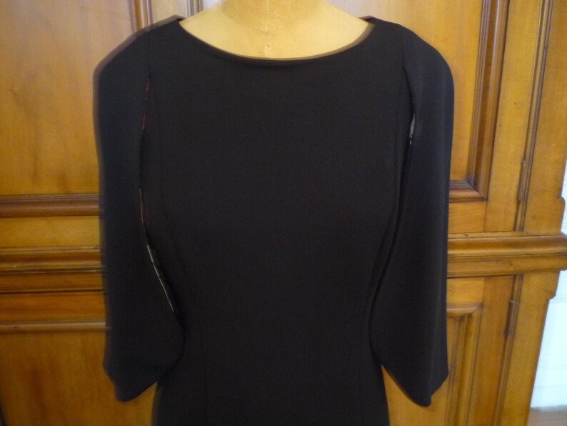 May include: A black dress with long sleeves and a round neckline. The sleeves have a unique design with a slight flare at the wrist.
