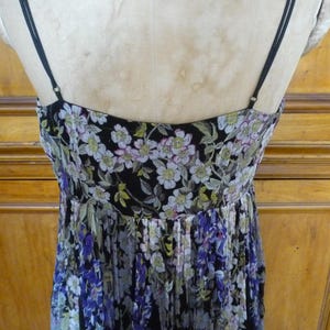 Puede incluir: Vestido con estampado floral y finas correas negras. El vestido presenta un fondo negro con un estampado de flores blancas, moradas y verdes. El vestido se exhibe en un maniqu&iacute;.