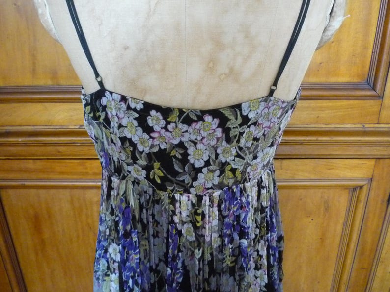 Puede incluir: Vestido con estampado floral y finas correas negras. El vestido presenta un fondo negro con un estampado de flores blancas, moradas y verdes. El vestido se exhibe en un maniqu&iacute;.