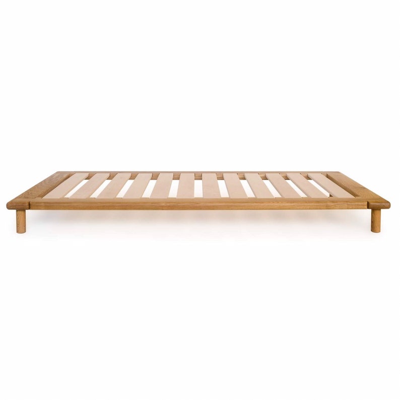 May include: A wooden bed frame with a slatted base and four legs. The frame is made of natural wood and has a light brown finish.