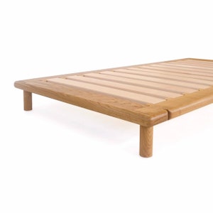 May include: A wooden bed frame with a slatted base and four legs. The frame is made of light brown wood and has a natural finish.