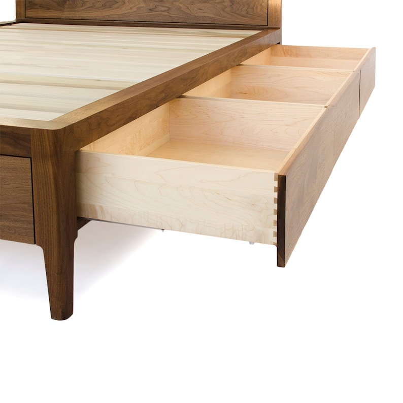 Peut inclure: Un cadre de lit en bois avec une t&ecirc;te de lit en bois clair et une base en bois fonc&eacute;. Le cadre de lit a trois tiroirs qui sont partiellement ouverts, r&eacute;v&eacute;lant un int&eacute;rieur en bois clair.