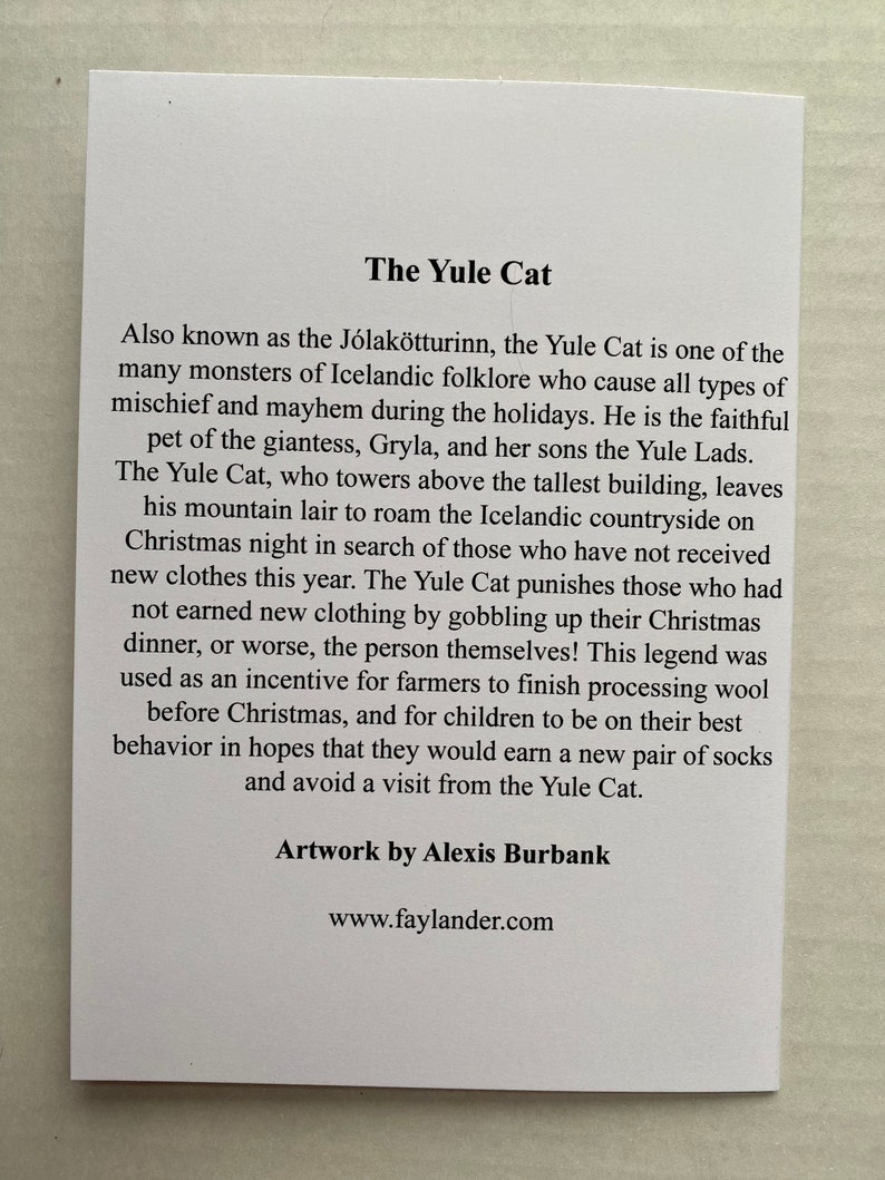May include: A white card with black text about the Yule Cat, a creature from Icelandic folklore. The text explains that the Yule Cat punishes those who don't receive new clothes for Christmas. The card also includes the text "Artwork by Alexis Burbank" and "www.faylander.com".