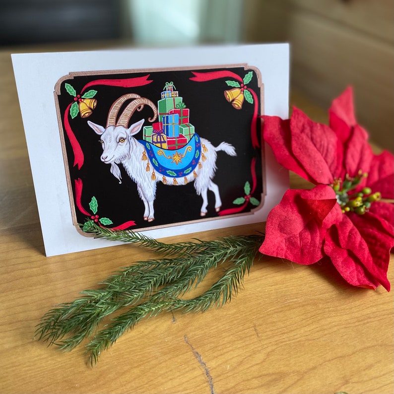 May include: A Christmas card featuring a white goat with gold horns carrying a stack of wrapped presents on its back. The goat is standing on a black background with red and green accents. The card has a festive design with holly and bells.