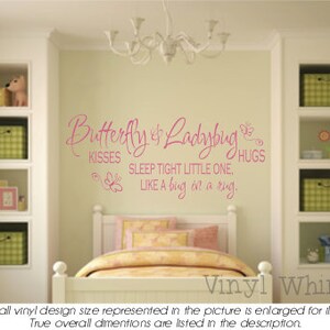 May include: Pink vinyl wall decal with the text "Butterfly & Ladybug Kisses Sleep Tight Little One, Like a bug on a ring. Hugs" in a cursive font. The decal is displayed on a white wall above a white bed with pink and white bedding.