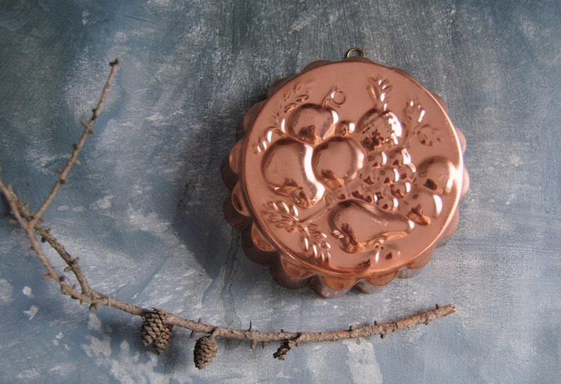 Peut inclure: Un moule &agrave; g&acirc;teau en cuivre avec un motif en relief de fruits et de feuilles. Le moule a un bord cannel&eacute; et une boucle de suspension.