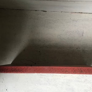 May include: A close-up of a red shelf, with a rough texture, against a white wall.
