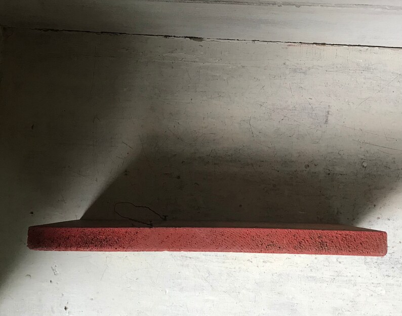 May include: A close-up of a red shelf, with a rough texture, against a white wall.