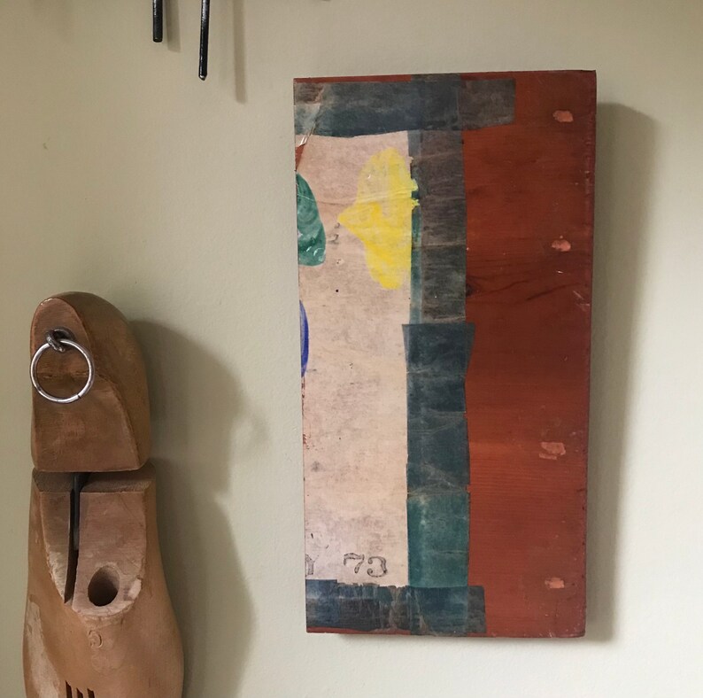 May include: A rectangular wooden panel with a layered, abstract design. The panel is painted in shades of brown, green, blue, and yellow. The number "73" is visible on the panel.