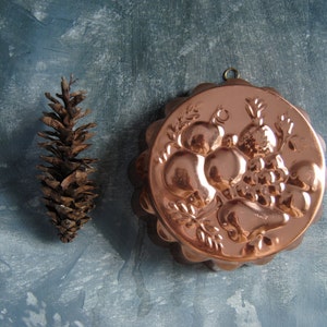 Peut inclure: Un moule &agrave; g&acirc;teau en cuivre avec un motif en relief de fruits et de feuilles. Le moule a un bord festonn&eacute; et une boucle de suspension.