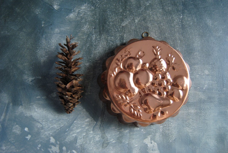 Peut inclure: Un moule &agrave; g&acirc;teau en cuivre avec un motif en relief de fruits et de feuilles. Le moule a un bord festonn&eacute; et une boucle de suspension.