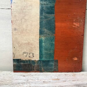 May include: A close-up of a wooden board with a white, blue, and red painted design. The board has a number "73" written on it.