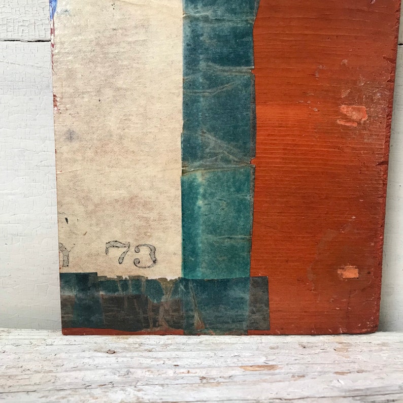 May include: A close-up of a wooden board with a white, blue, and red painted design. The board has a number "73" written on it.