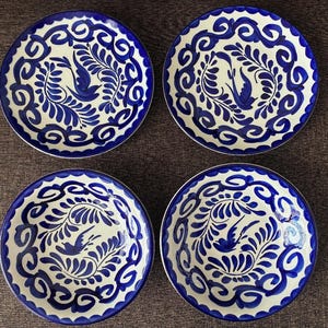 May include: Four ceramic plates featuring white bases and detailed blue floral and bird patterns. The plates have a scalloped edge and are arranged in a square. These plates are suitable for serving food.