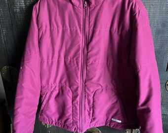 May include: A magenta puffer jacket with a high collar and a full-length zipper. The jacket has a quilted design and two front pockets. The jacket is hanging on a metal hanger.