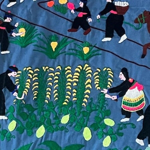 以下が含まれることがあります： カラフルな刺繍が施された壁掛けで、畑で働く人々の様子が描かれています。人々は伝統的な服装をし、植物や花に囲まれています。背景は薄い青色です。