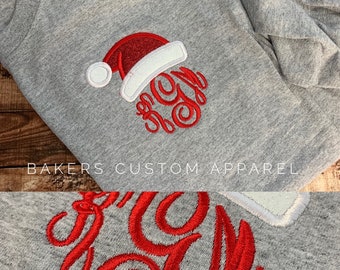 May include: A gray sweatshirt with a red embroidered Santa hat and monogram. The text "BAKERS CUSTOM APPAREL" is printed below the monogram.