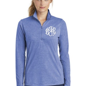 May include: A blue long-sleeved shirt with a white monogram on the chest. The shirt has a zippered collar and a heather-like texture.
