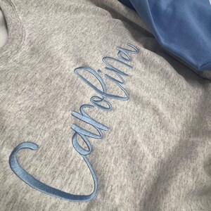 May include: A grey sweatshirt with the word "Carolina" embroidered in light blue cursive lettering.