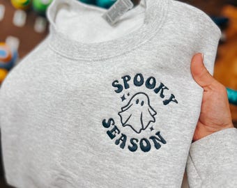 Puede incluir: Una sudadera gris con un diseño bordado en negro de un fantasma y el texto "Spooky Season".