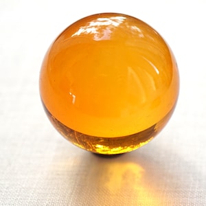 Peut inclure: Un presse-papier rond en verre orange avec une surface lisse et brillante.