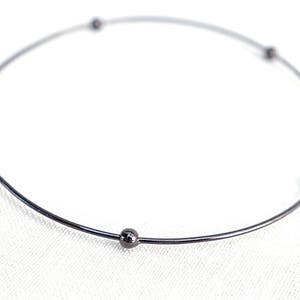 Op de afbeelding: Een zwarte metalen armband met vijf kleine ronde kralen.