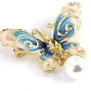 May include: A gold-tone butterfly brooch with blue and white enamel and clear rhinestones. A white pearl dangles from the bottom of the brooch.