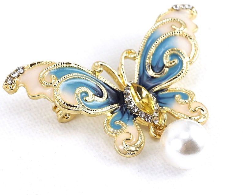 May include: A gold-tone butterfly brooch with blue and white enamel and clear rhinestones. A white pearl dangles from the bottom of the brooch.