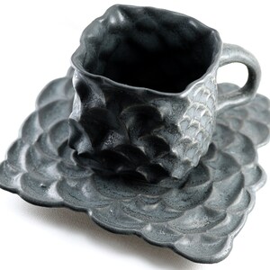 May include: A dark gray ceramic teacup and saucer set with a textured, wave-like design.