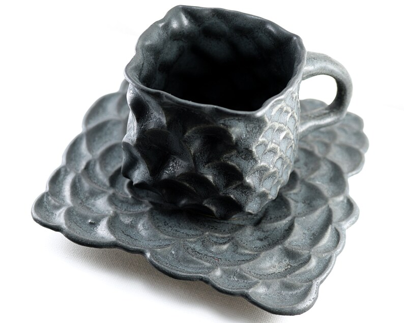 May include: A dark gray ceramic teacup and saucer set with a textured, wave-like design.