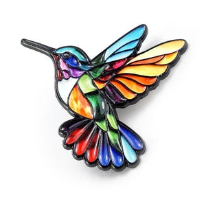 May include: A colorful hummingbird pin with a black outline. The bird's wings and body are segmented with vibrant colors including blue, green, orange, yellow, and red. The pin is set against a white background.