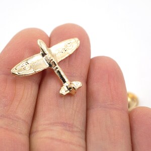 Puede incluir: Un pin de metal de color dorado con forma de avi&oacute;n vintage. El avi&oacute;n tiene un dise&ntilde;o detallado y es un objeto de colecci&oacute;n popular.