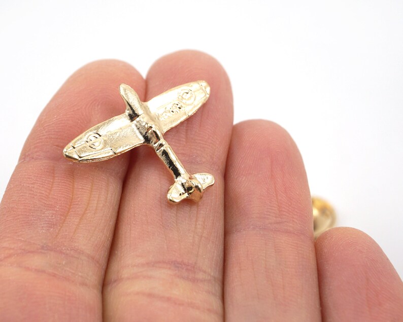 Puede incluir: Un pin de metal de color dorado con forma de avi&oacute;n vintage. El avi&oacute;n tiene un dise&ntilde;o detallado y es un objeto de colecci&oacute;n popular.