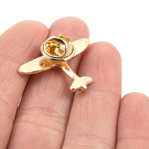 Puede incluir: Pin de avi&oacute;n dorado con cierre de seguridad. El pin tiene la forma de un avi&oacute;n peque&ntilde;o con una h&eacute;lice.