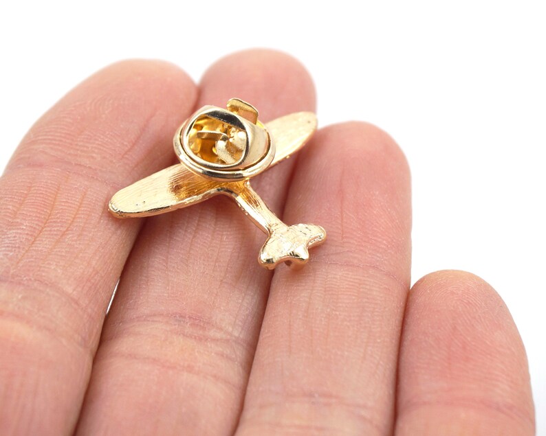 Puede incluir: Pin de avi&oacute;n dorado con cierre de seguridad. El pin tiene la forma de un avi&oacute;n peque&ntilde;o con una h&eacute;lice.