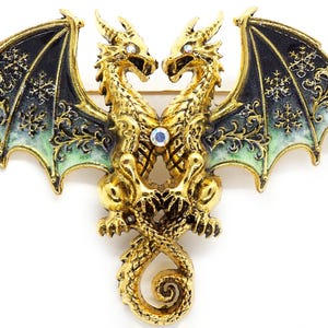 May include: A gold-toned dragon brooch featuring two intertwined dragons with outstretched wings. The wings are black with green and white accents and snowflake-like patterns. The brooch is adorned with rhinestones.