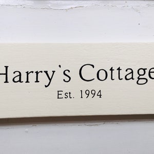 Pode incluir: Placa de madeira branca com texto preto que diz "Harry's Cottage Est. 1994".