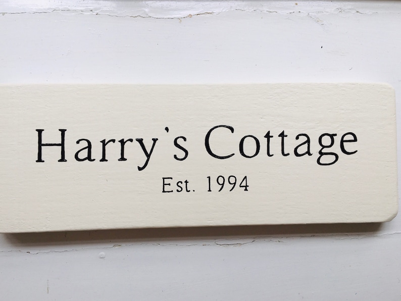 Pode incluir: Placa de madeira branca com texto preto que diz "Harry's Cottage Est. 1994".