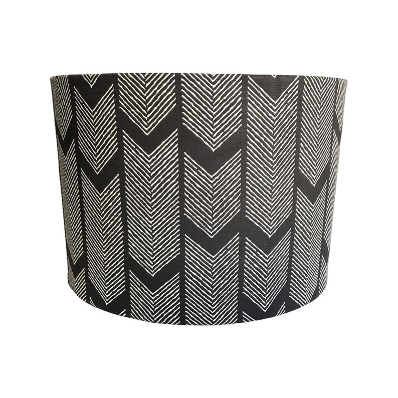 May include: Black and white chevron patterned lampshade. The lampshade is cylindrical and has a white background with black chevron patterns.