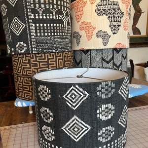 May include: Four lampshades with different geometric patterns. The lampshades are black, brown, and white with geometric patterns. The lampshades are stacked on top of each other.