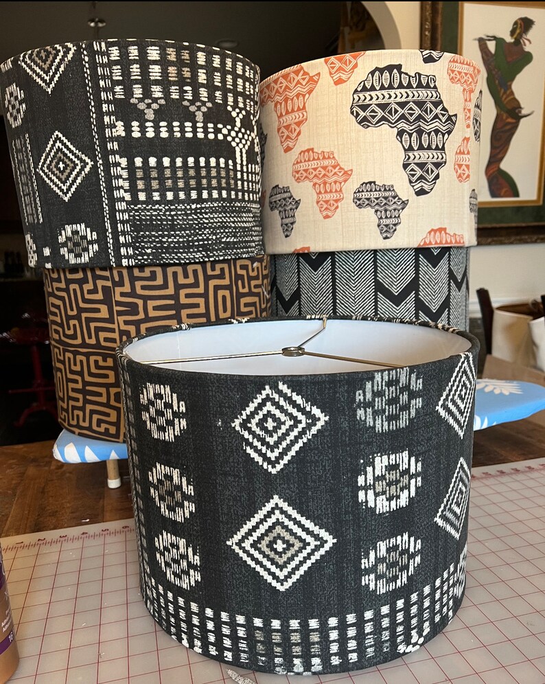 May include: Four lampshades with different geometric patterns. The lampshades are black, brown, and white with geometric patterns. The lampshades are stacked on top of each other.