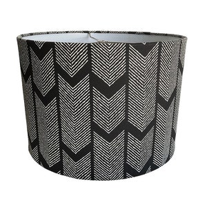May include: Black and white lampshade with a chevron pattern. The lampshade is cylindrical and has a white interior.
